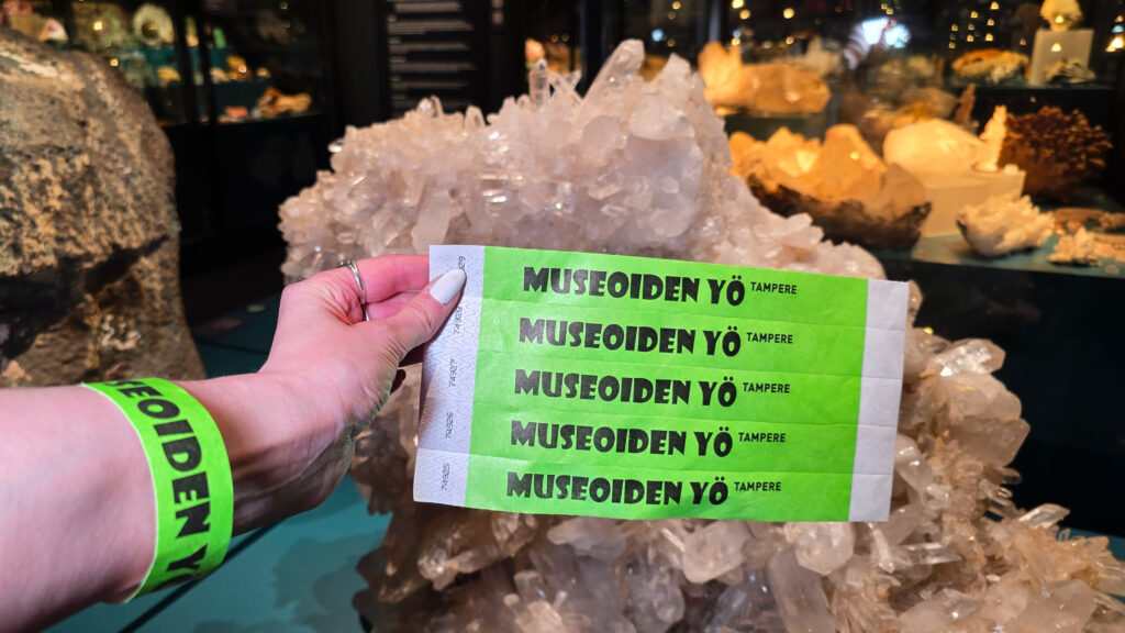 Bright green "Night of the Museums" wristbands take center stage in the photo, with minerals visible in the dimly lit exhibition space in the background.